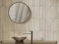 Un lavabo moderne et un miroir rond se reflètent sur un mur de toilette carrelage aux tons sable.