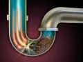 Tuyau de douche bouché avec accumulation de saleté, causant une mauvaise odeur. Des flèches rouges indiquent un flux bloqué.