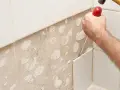 Main d'un bricoleur en pleine action pour enlever carrelage mural avec un burin et un marteau. La surface est prête pour un nouveau revêtement.