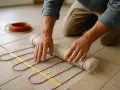 Pose d'un tapis chauffant pour plancher avant la pose de la colle carrelage. Un rouleau de câble rouge est visible.