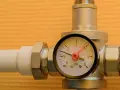 Un réducteur de pression d'eau avec un manomètre indiquant 1 bar. L'appareil est monté sur un tuyau blanc.