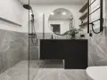 Salle de bain moderne avec douche à l'italienne, meuble suspendu noir, miroir rond et carrelage effet marbre. La construction de cette salle de bain est soignée.