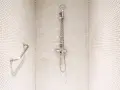 Douche moderne avec carrelage blanc en mosaïque. Une barre d'appui chromée et un pommeau de douche argenté se détachent sur le fond. Le receveur noir est discret.