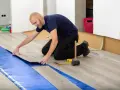 Pose d'un revêtement de sol stratifié sur une sous-couche d'isolation phonique sous carrelage. Outils de pose à proximité.