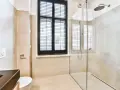 Salle de bain moderne avec douche à l'italienne, carrelage beige, fenêtre à persiennes noires et WC suspendu.