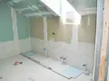 Chantier de salle de bain : murs en plaques de plâtre, tuyauterie apparente, niveau à bulle et outils au sol. Travaux d'isolation salle de bain en cours.