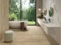 Salle de bain moderne avec baignoire îlot, double vasque en marbre et **pose carrelage imitation parquet** au sol et sur un mur. Vue sur jardin luxuriant.