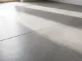 Gros plan sur un carrelage gris moderne, baigné de lumière. On entendrait presque le carrelage qui sonne creux sous les pas.