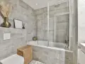 Salle de bain entierement carrelée de gris, avec baignoire, douche, lavabo et WC. Un panier en osier et des herbes séchées apportent une touche naturelle.
