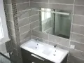 Salle de bain moderne avec double vasque. Le carrelage sol gris, posé au mur, crée une ambiance élégante.