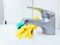 Gants jaunes et éponge verte prêts pour nettoyer robinetterie entartrée.