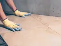 Pose de carrelage : mains gantées ajustant une nouvelle dalle sur la sous couche carrelage.