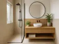 Douche moderne et meuble vasque en bois dans une petite salle de bain 3m2. Miroir rond, plantes vertes et carrelage clair apportent une touche zen.