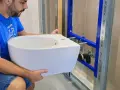 Un homme installe un bidet blanc, un élément essentiel pour une hygiène intime.