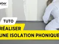 Tuto : réaliser une isolation phonique sur carrelage existant. Un ouvrier en combinaison blanche installe un revêtement gris au sol.