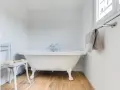 Baignoire îlot blanche sur pieds, robinetterie argentée. La hauteur baignoire est standard, avec un petit tabouret à côté.