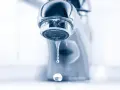 Gouttelettes d'eau tombant d'un robinet de salle de bain qui fuit. Un petit désagrément qui coûte cher.