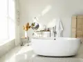Salle de bain lumineuse avec baignoire îlot blanche, lavabo, miroir, porte-serviettes et paravent en bois. La largeur d'une baignoire est parfaite pour ce coin détente.