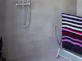 Salle de bain béton ciré aux tons gris, avec une douche chromée et un porte-serviettes orné d'une serviette rayée.
