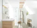 Salle de bain lumineuse avec douche, lavabo en bois clair et paniers de rangement. Un style de wet room épuré et naturel.