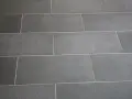 Détail d'un sol en carrelage gris anthracite, avec un joint carrelage couleur crème qui souligne la pose rectiligne.