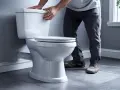 Un homme ajuste le couvercle d'un nouveau **pose wc** blanc, prêt pour l'installation.