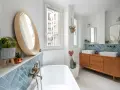 Salle de bain moderne avec carrelage zellige bleu canard, baignoire, double vasque sur meuble vintage et miroir rond en bois. Inspiration zellige.