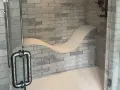 Douche moderne avec un banc ondulé intégré dans le mur de briques. La poignée de la porte en verre est en métal vieilli.