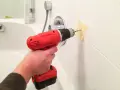 Main tenant utilise une perceuse pour percer le carrelage de la salle de bain, afin d'y fixer un accessoire.