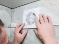 Mains d'homme ajustant une grille de VMC dans une salle de bain car une mauvaise odeur persiste.