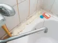 Mousse expansive appliquée pour nettoyer joint plastique porte douche. Savon et bouchon de bain à proximité.