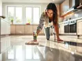 Une femme nettoie son carrelage de cuisine avec un produit pour le faire briller. Le sol reflète la lumière des fenêtres.