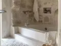 Une **salle de bain méditerranéenne** avec baignoire en pierre brute, robinetterie moderne et serviette blanche suspendue. Ambiance zen.