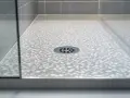 Bac de douche moderne avec motif de bulles et grille d'évacuation. La paroi vitrée reflète la lumière.