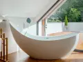 Baignoire design en matière composite, avec robinetterie chromée, devant une grande baie vitrée donnant sur un jardin luxuriant.