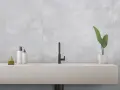 Évier moderne avec robinetterie noire, flacons de savon et plante verte, sur un mur en carrelage rectifié gris.