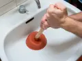 Main tenant utilise une ventouse pour déboucher un lavabo bouché.