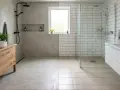 Salle de bain moderne avec sol en béton ciré ou résine d'un côté, et carrelage de l'autre. Douche vitrée, meuble vasque en bois.