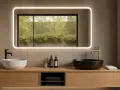 Élégante salle de bain feng shui avec deux vasques, robinetterie dorée et noire, et un miroir lumineux reflétant la verdure extérieure.
