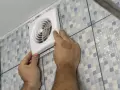 Mains d'un homme installant un ventilateur, une étape clé pour une bonne installation VMC dans une salle de bain carrelée.