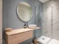 Aménagement petite salle de bain : meuble suspendu en bois clair, vasque ronde, miroir rond, douche à l'italienne.