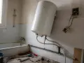 Un chauffe-eau blanc est en cours de branchement dans une salle de bain. Des outils sont posés sur le sol.