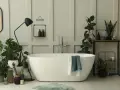Une salle de bain baignée de lumière, avec une baignoire blanche, de nombreuses plantes vertes qui prospèrent dans l'humidité, et un miroir ovale.