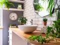 Comment décorer une salle de bain : un lavabo rond sur un meuble en bois, entouré de plantes vertes luxuriantes et d'un miroir mural.