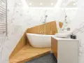 Salle de bain moderne avec baignoire îlot sur une estrade en bois, lavabo, miroir et carrelage marbre.