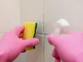 Main rose gantée tient une éponge jaune pour nettoyer une tache sur carrelage qui ne part pas.