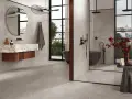 Salle de bain moderne avec baignoire îlot et douche vitrée. Le sol et les murs sont recouverts de carrelage gris, tandis que la paroi de douche est en petite faïence.