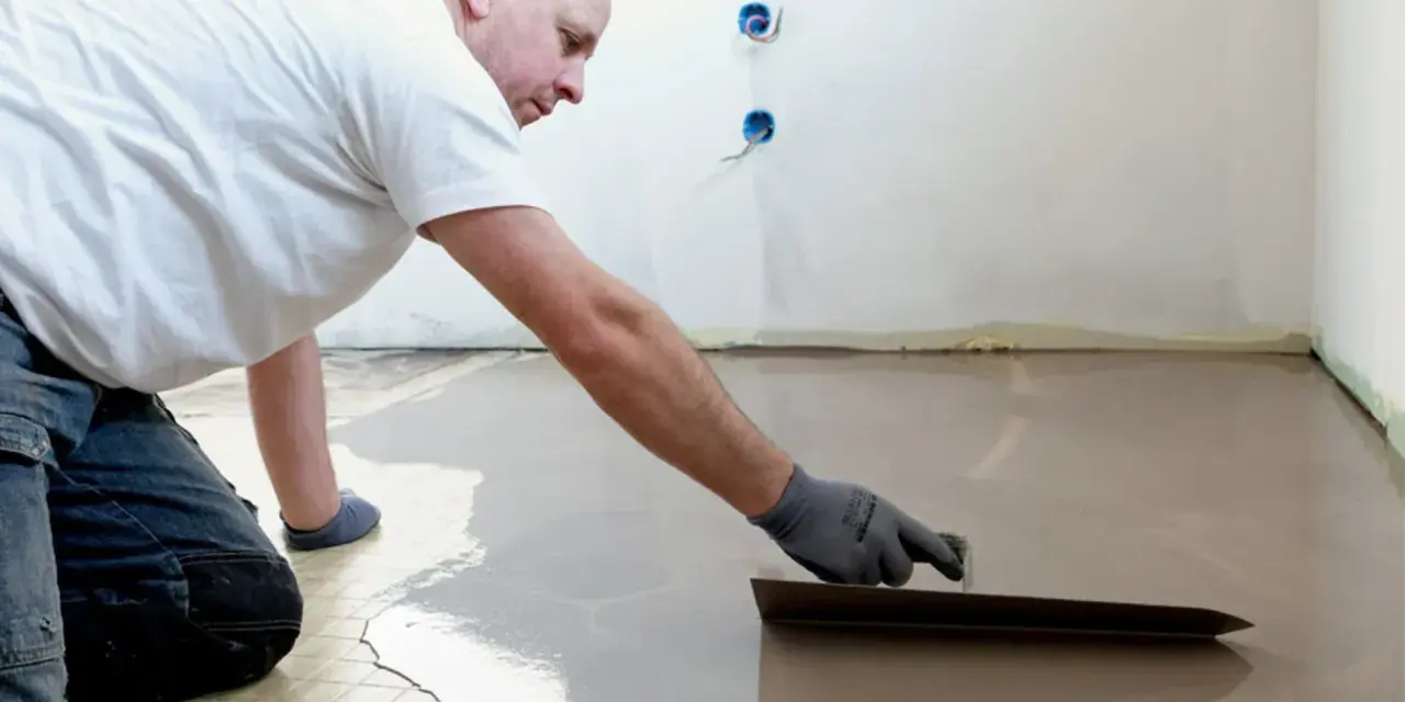 Un ouvrier applique du ragréage autonivelant sur un sol, créant une surface lisse et uniforme.