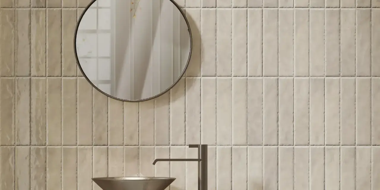 Un lavabo moderne et un miroir rond se reflètent sur un mur de toilette carrelage aux tons sable.