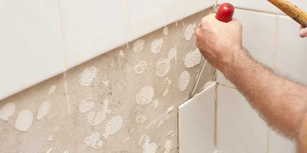 Main d'un bricoleur en pleine action pour enlever carrelage mural avec un burin et un marteau. La surface est prête pour un nouveau revêtement.